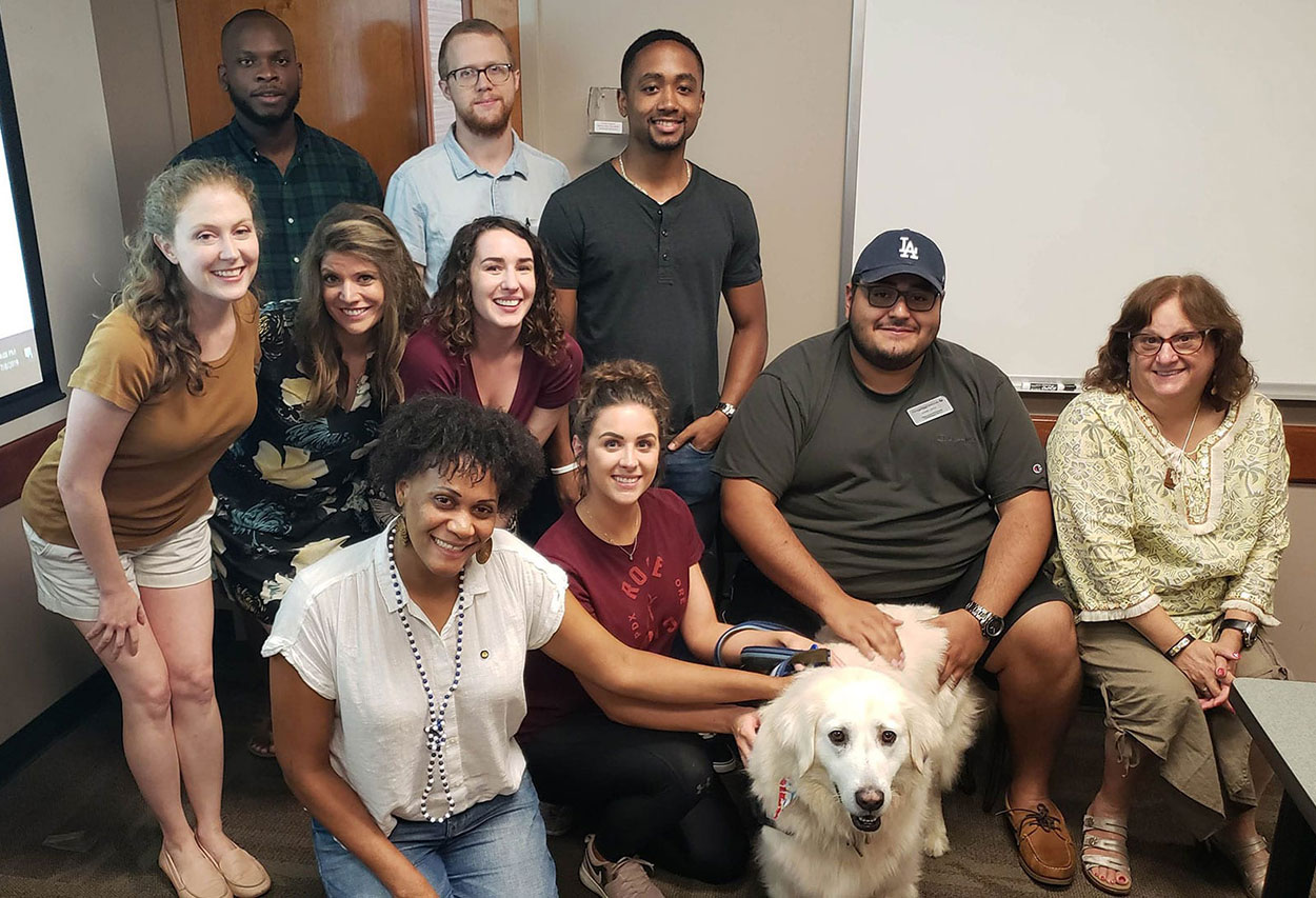 A group of people pose and pet a dog